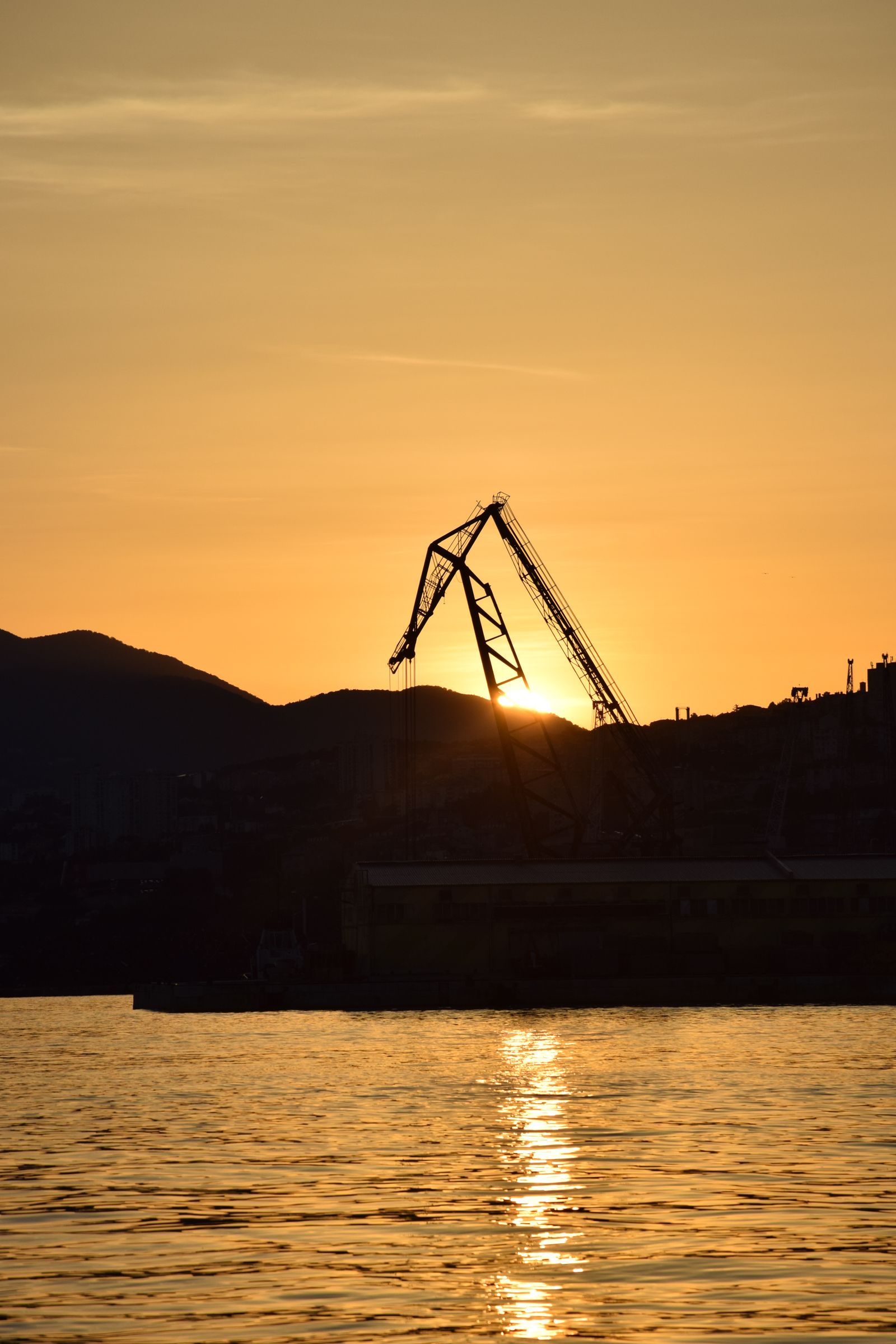A harbour crane silhouetted against a golden sunset — illustrative photography