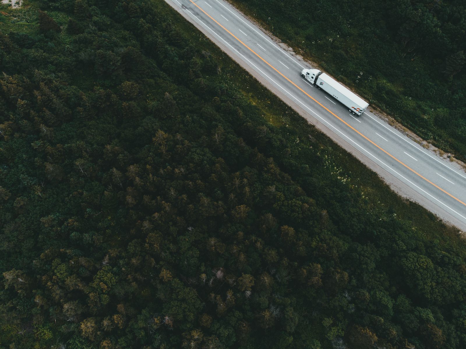 A haulage truck on an open highway cutting through forest, seen from above — illustrative photography